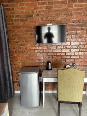 a tv on a brick wall with a table and chair at Glowti Event & Guest House in Centurion