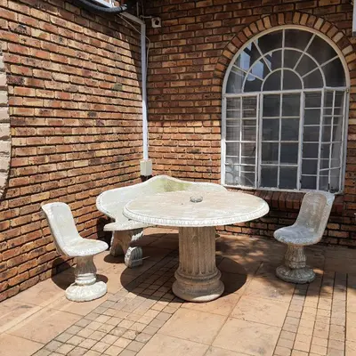 a stone table and two chairs in front of a brick wall at Oppiplot Guest House Pty Ltd in Kempton Park