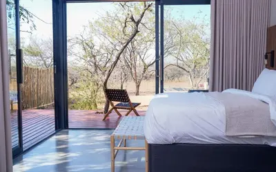 a bedroom with a bed and a chair on a deck at Amani Luxury Villa Marloth Park in Marloth Park