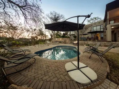 a swimming pool with two chairs and an umbrella at 8 On Penny Guesthouse in Nelspruit