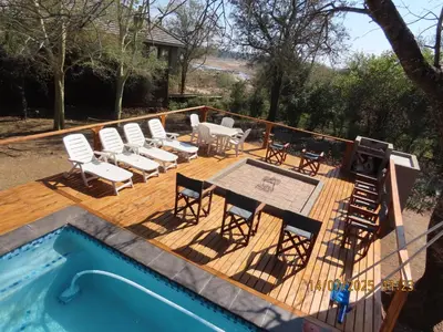 a deck with chairs and a table next to a pool at Luxury GuesthouseCo RiverBend in Marloth Park