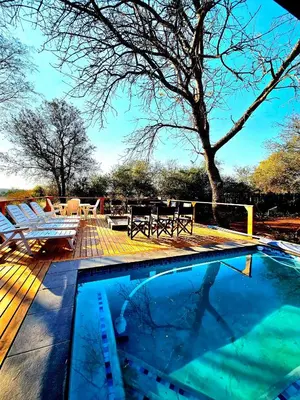 a swimming pool with a table and chairs on a deck at Luxury GuesthouseCo RiverBend in Marloth Park