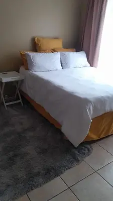 a bed with white sheets and pillows and a table at Home away from home in Polokwane