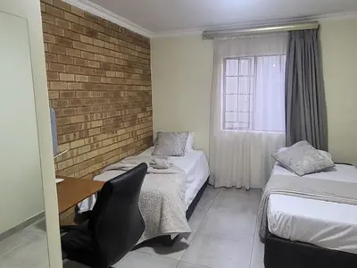a room with two beds and a desk and a window at Mhlahlo Guests in Ga-Rankuwa