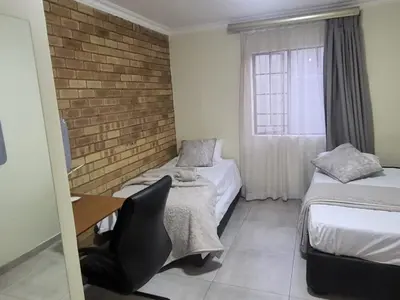 a room with two beds and a desk and a window at Mhlahlo Guests in Ga-Rankuwa