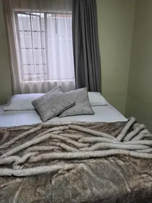a bed with a blanket and pillows with a window at Mhlahlo Guests in Ga-Rankuwa
