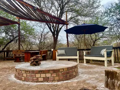 a fire pit with two chairs and an umbrella at Kudu's Corner in Marloth Park
