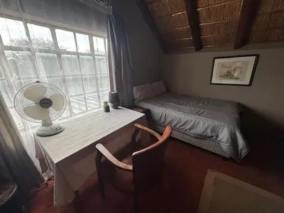 a bedroom with a bed and a desk with a fan at Kudu's Corner in Marloth Park