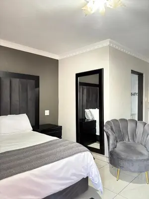 a bedroom with a bed and a chair and a mirror at Nyakhosi Luxury Guesthouse in Thohoyandou
