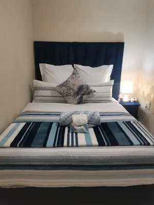 a bed with a blue headboard and white pillows at The Glenwood RRR Guesthouse in Midrand