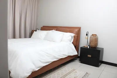 a bedroom with a bed with white sheets and a night stand at Blue Lake Estate Home in Midrand