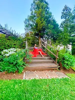 a woman in a red dress sitting on a wooden stairs at Tranquil view lodge in Haenertsburg