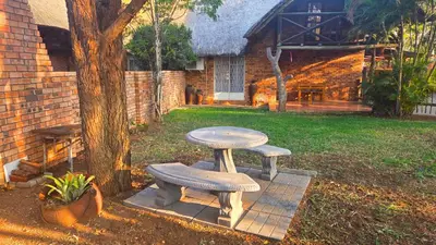 a picnic table and two benches next to a tree at Dika Dika Den in Phalaborwa
