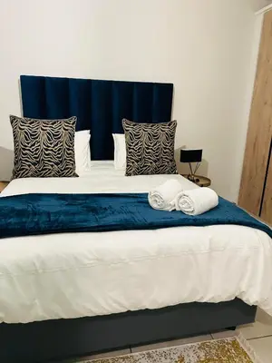 a large bed with blue and white sheets and pillows at The Corinthians in Pretoria