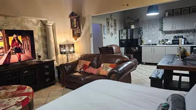 a living room with leather furniture and a kitchen at Rose Vintage Cottage in Pretoria