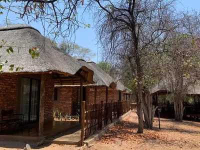 a brick building with a thatched roof and a fence at Moyo Safari Lodge in Alldays