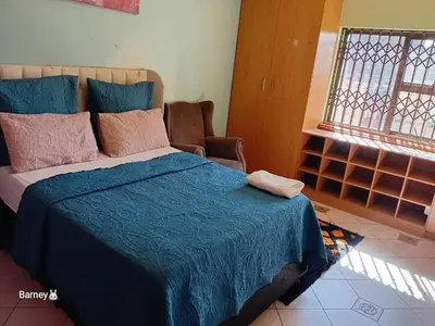 a bedroom with a bed with a blue blanket and a chair at M Palace Guest House in Kempton Park