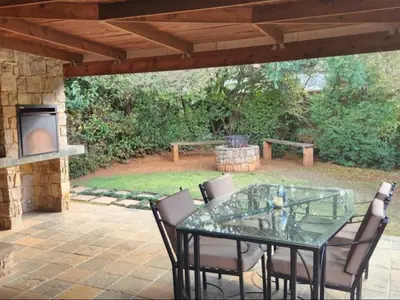 a glass table and chairs on a patio with a fireplace at Big Oak Cottages in Dullstroom