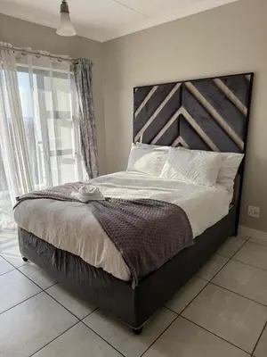 a bedroom with a large bed with a wooden headboard at Penthouse On Tropical - The Blyde in Pretoria