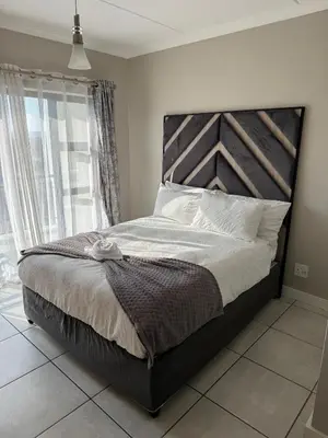 a bedroom with a large bed with a wooden headboard at Penthouse On Tropical - The Blyde in Pretoria