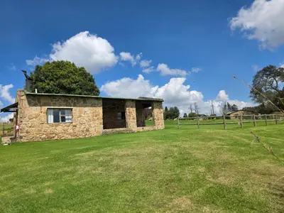 a stone building in a field with a fence at Treeferns Trout Lodge in Dullstroom