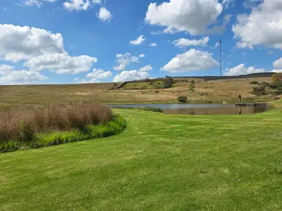 a golf course with a pond and a grass field at Treeferns Trout Lodge in Dullstroom