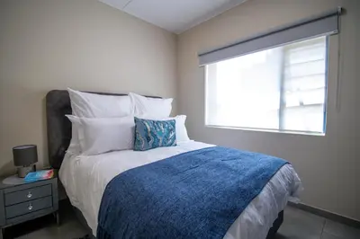 a bedroom with a bed with a blue blanket and a window at Waterfall Ridge Luxurious Apartments - Backup Power! in Midrand