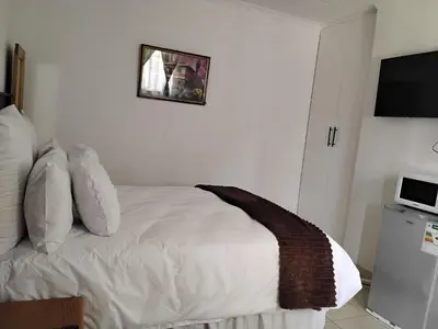 a bedroom with a bed with white sheets and a television at Best Enough Guesthouse in Pretoria