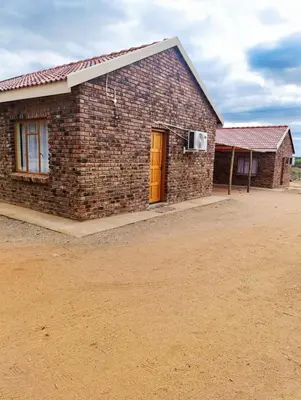 a brick house with a red door on a dirt field at Lapa Moyo Safari's in Linton