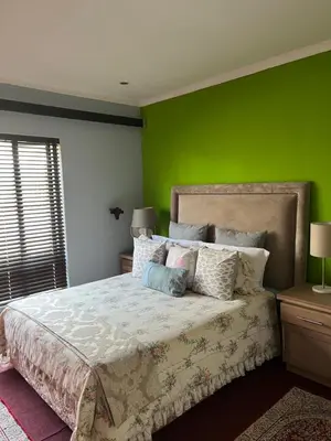a bedroom with green walls and a bed with pillows at Nzwaki Self Catering in Nelspruit