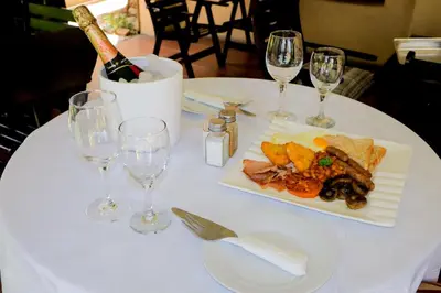a white table with a plate of food and wine glasses at Masai Shuttles And Hotel in Polokwane