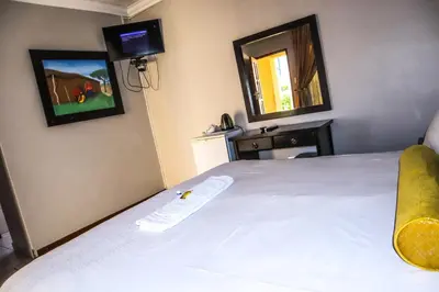 a bedroom with a white bed and a mirror at Masai Shuttles And Hotel in Polokwane