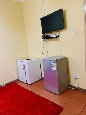 a room with two refrigerators and a tv on the wall at Galaxy Guesthouse Pretoria North in Pretoria