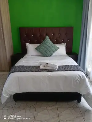 a large bed with a green headboard and white sheets at House 224 Lodge in Driekop