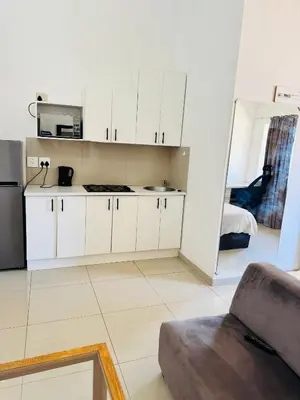 a kitchen with white cabinets and a couch in a room at Airport Guest House in Kempton Park