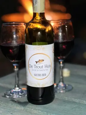 a bottle of wine sitting on a table with two glasses at De Trout Huis Guesthouse in Dullstroom