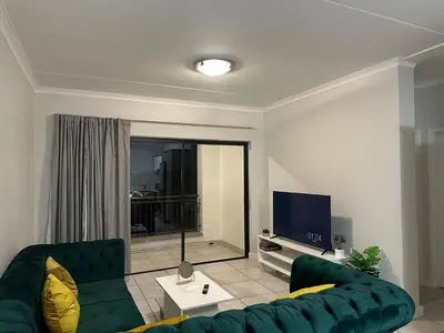 a living room with a green couch and a tv at The Blyde - Stay Iconic 2 bed Apartment in Pretoria