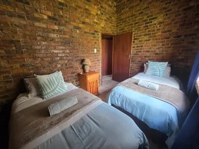 a bedroom with two beds and a brick wall at Treeferns Trout Lodge in Dullstroom