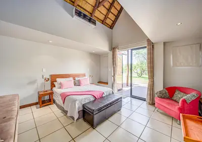 a bedroom with a bed and a red chair at Bush Lodge Zebula 82 - 2 x 2B Chalets in Warmbaths