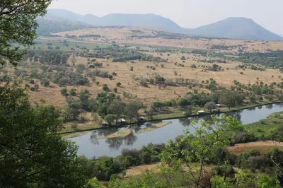 a river in a field with mountains in the background at Oppiberg Cottage with River View in Hartbeespoort