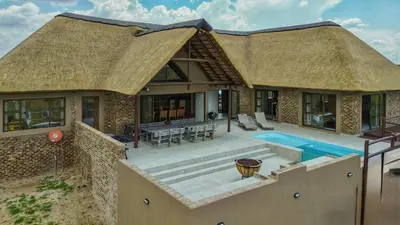a house with a thatched roof with a swimming pool at Pezulu Lodge in Warmbaths