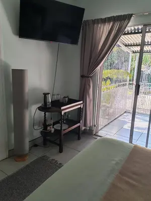 a bedroom with a bed and a table and a balcony at Be Our Guest Near OR Tambo International Airport 2 in Boksburg