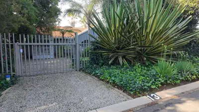 a fence with a plant in front of a yard at Be Our Guest Near OR Tambo International Airport 2 in Boksburg