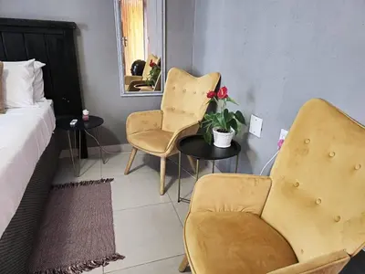 a bedroom with a bed and two chairs and a mirror at Akwaaba Fie Guesthouse in Lebowakgomo