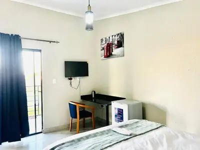 a bedroom with a bed and a desk and a television at TLS Cottages in Buffelspruit