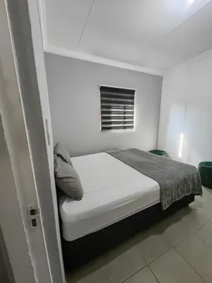 a small white bedroom with a bed and a window at Calm Corner in Pretoria
