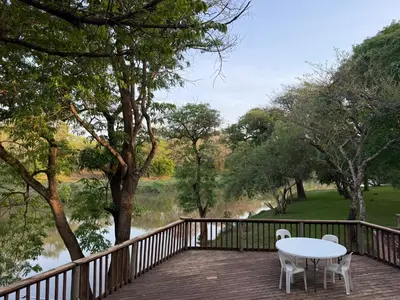 a wooden deck with a table and chairs and a river at Elephant 1 Chalet Hippo Waterfront Lodge in Nelspruit