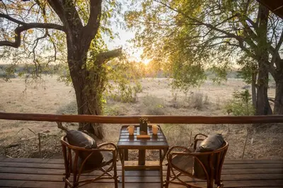 a table and chairs on a deck with a tree at Karongwe - Chisomo Safari Camp in Hoedspruit
