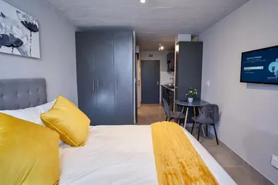 a bedroom with a bed with a yellow pillow and a table at Spacious Fully Equipped Studio - Peaceful-Free WiFi in Pretoria