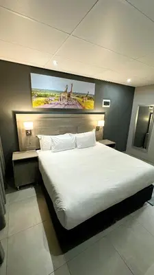 a bedroom with a large white bed with a painting on the wall at Khayalami Hotel - Secunda in Secunda